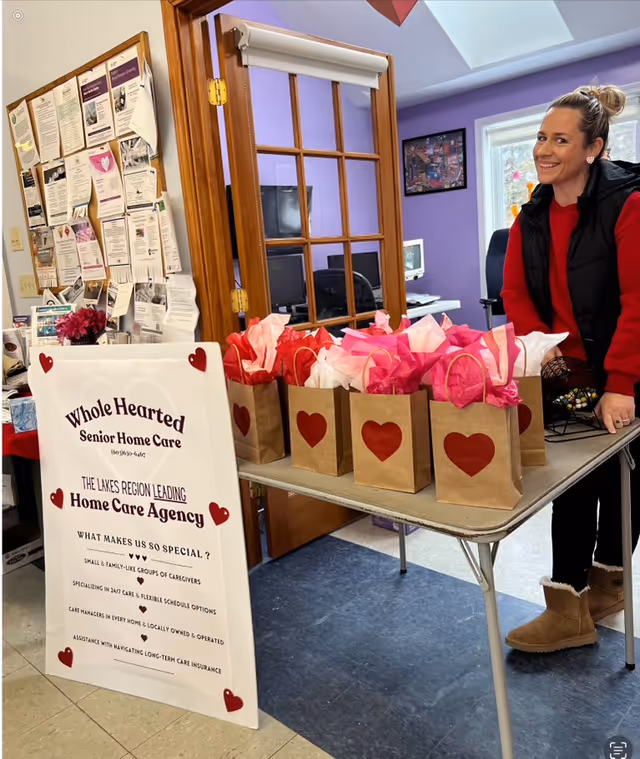 Caregiver stands beside table with heart gift bags and Whole Hearted Senior Home Care sign.