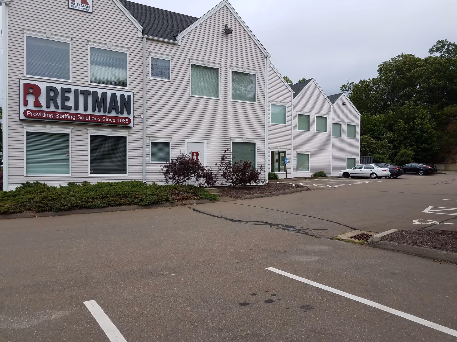 Light gray office building with a large REITMAN sign and surrounding parking lot.