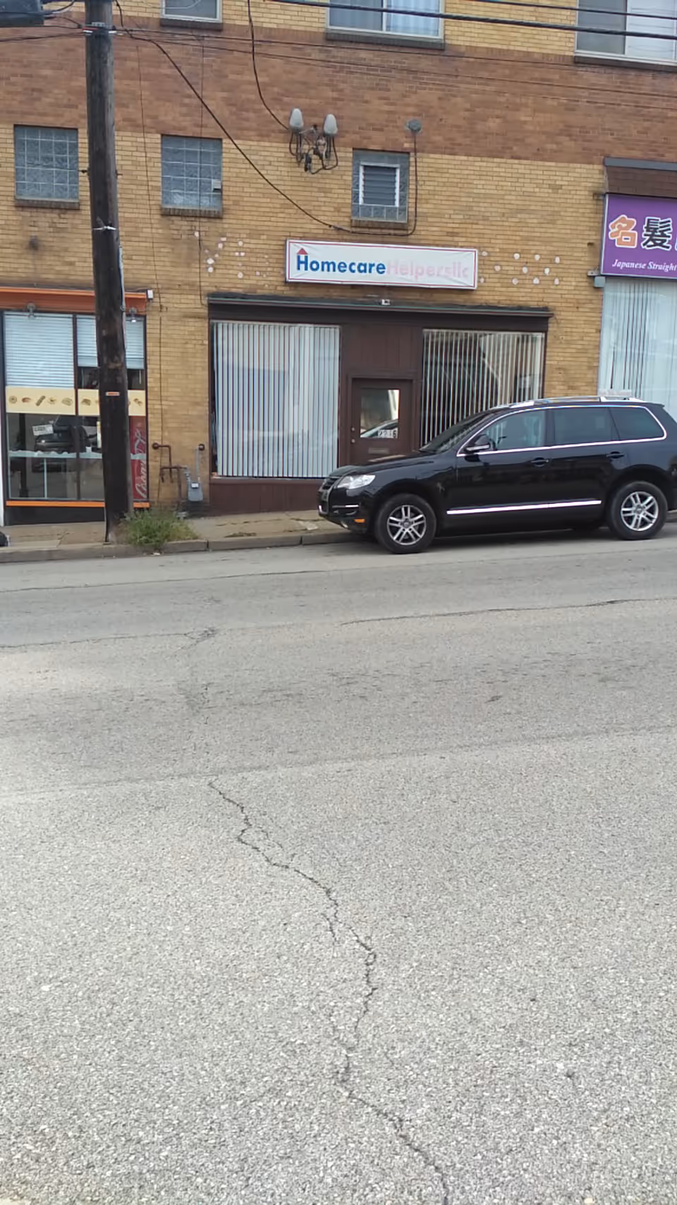 Exterior of brick storefront reading Homecare Helpers LLC with a black SUV parked outside.
