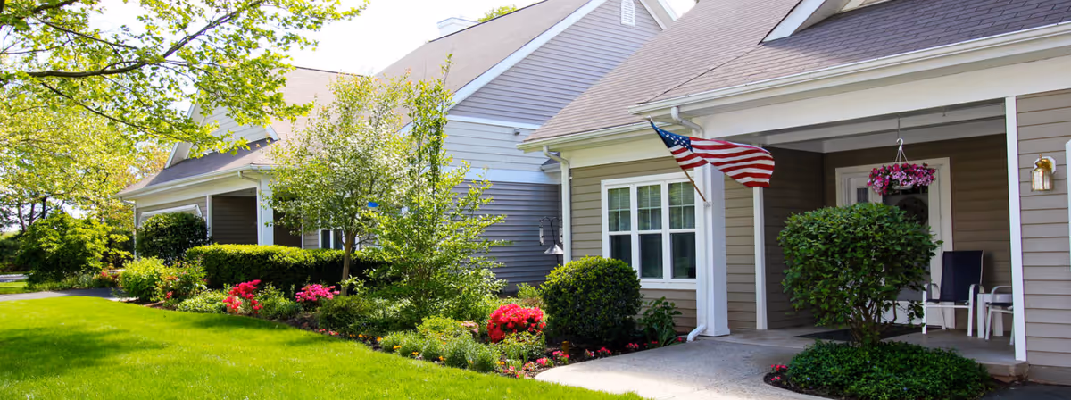 Well-maintained row of single-story senior living homes with porches, an American flag, and manicured lawn and flower beds.