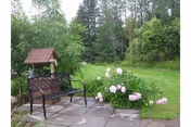 Outdoor seating area with a bench, small roofed shelter, and pink roses.