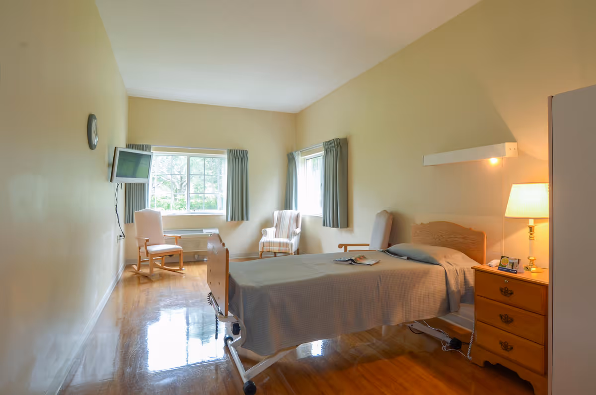 A furnished senior living bedroom with bed, chairs, and a window.