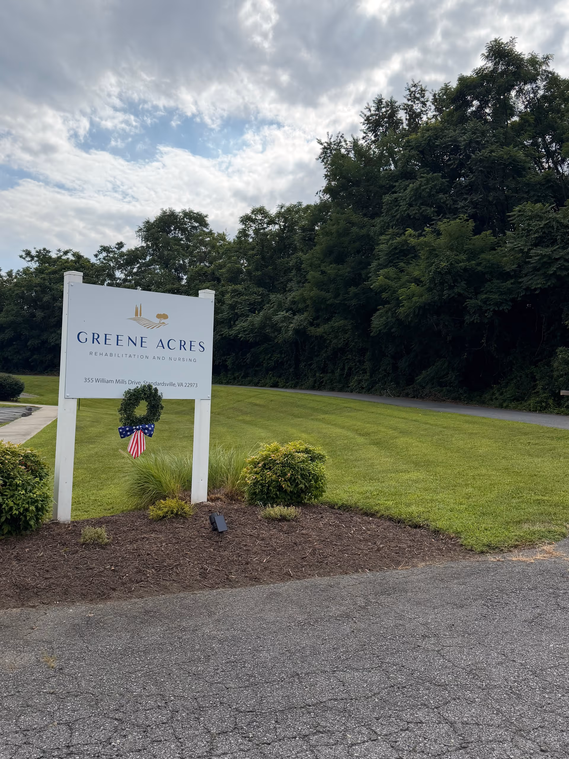 A white sign reading Greene Acres Rehabilitation and Nursing on a grassy front lawn.
