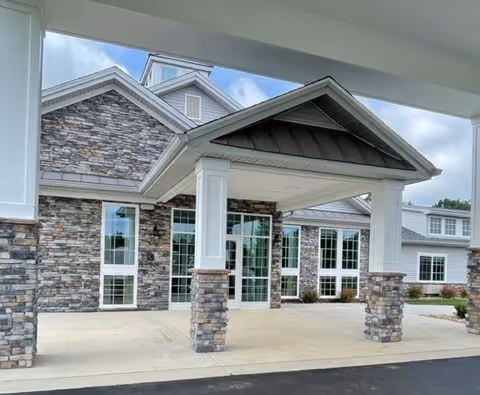 Stone-clad senior living facility entrance with columns and a covered drop-off area.