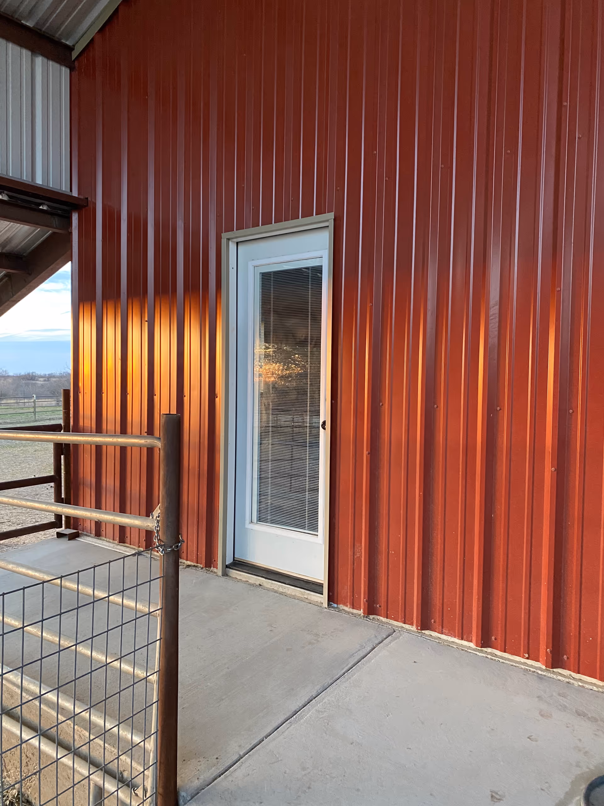 Red metal exterior wall with a glass-panel door and concrete ramp.
