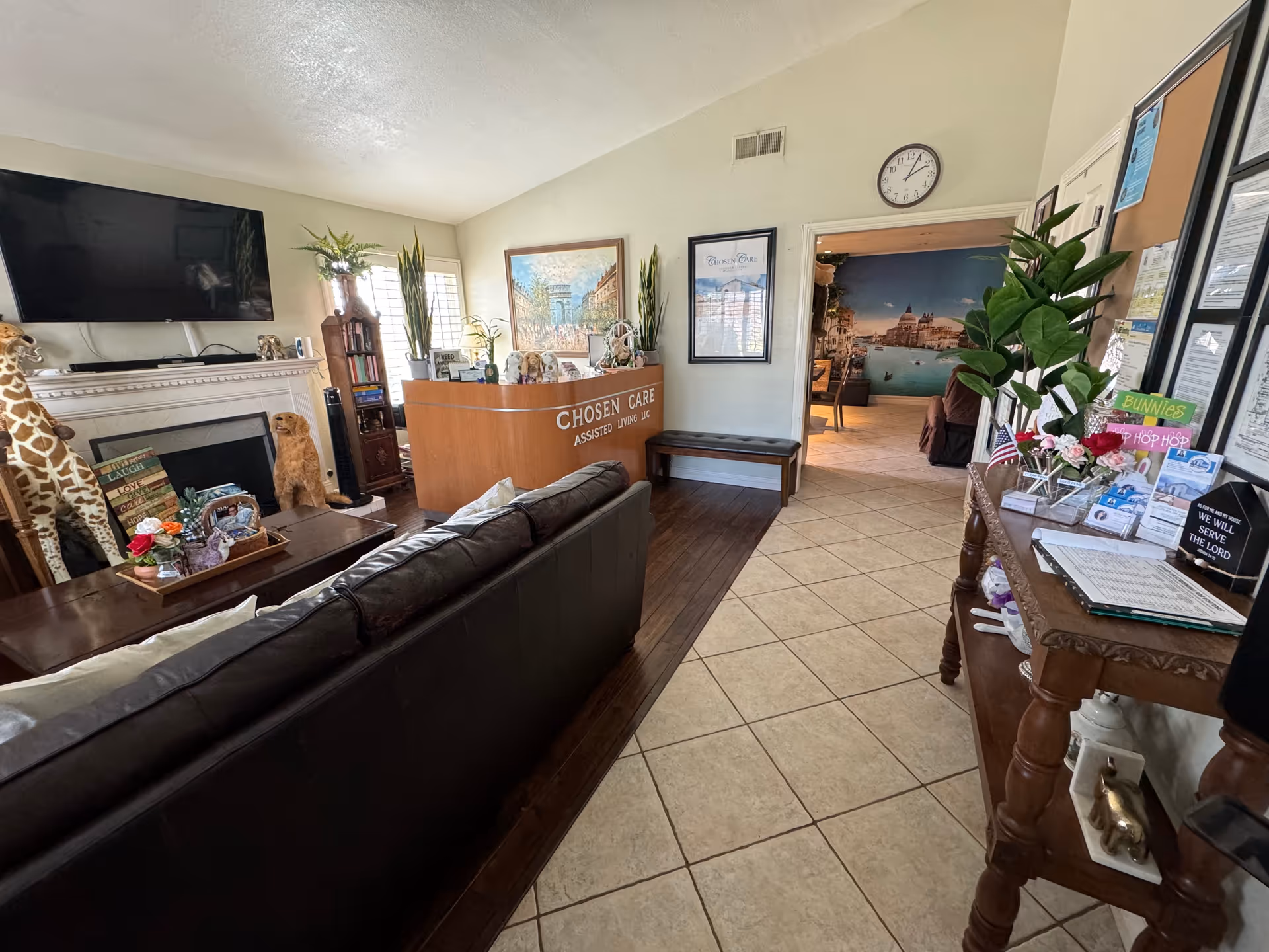 Reception lobby with curved wood desk, leather sofa, TV, plants, and art.