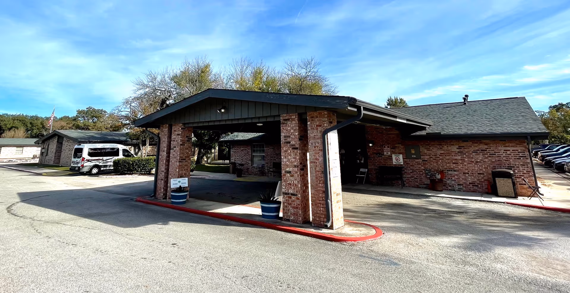 Brick senior living facility entrance under a wide black-roofed canopy with a van nearby.