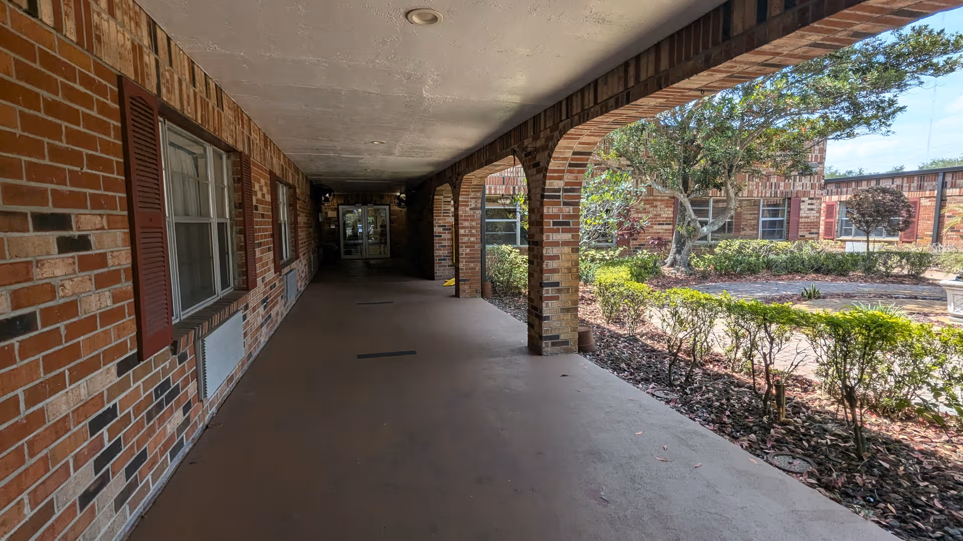 Covered brick walkway with arches and landscaping along a senior living facility