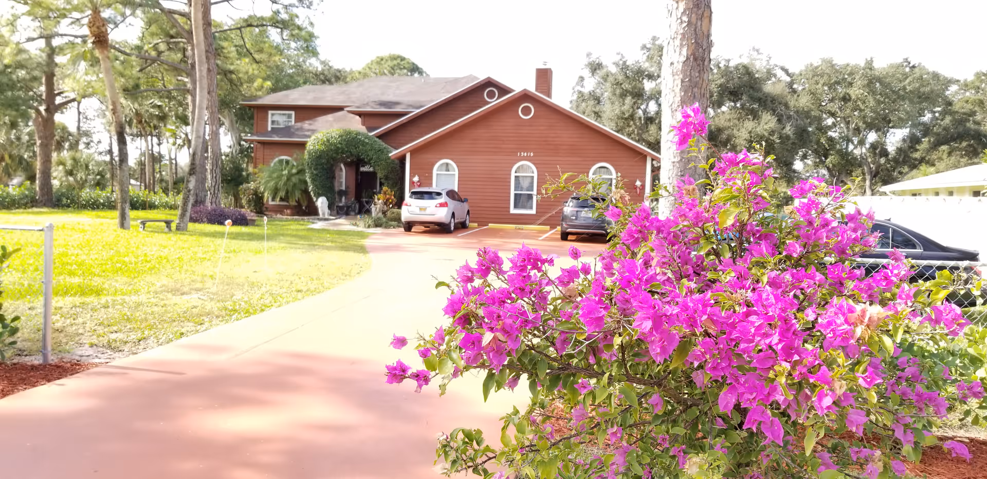 Front view of a brown building with parked cars and bright pink flowers.