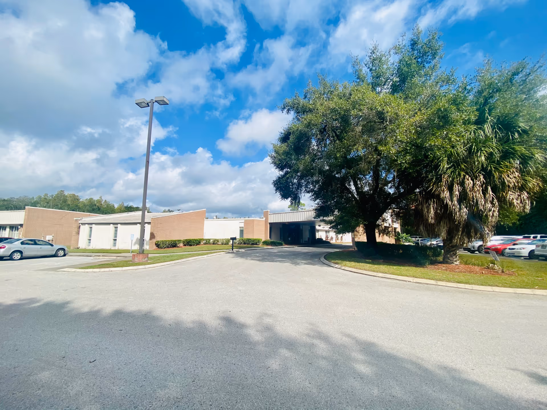 Exterior view of Carrollwood Care Center entrance with trees, parking, and blue sky.