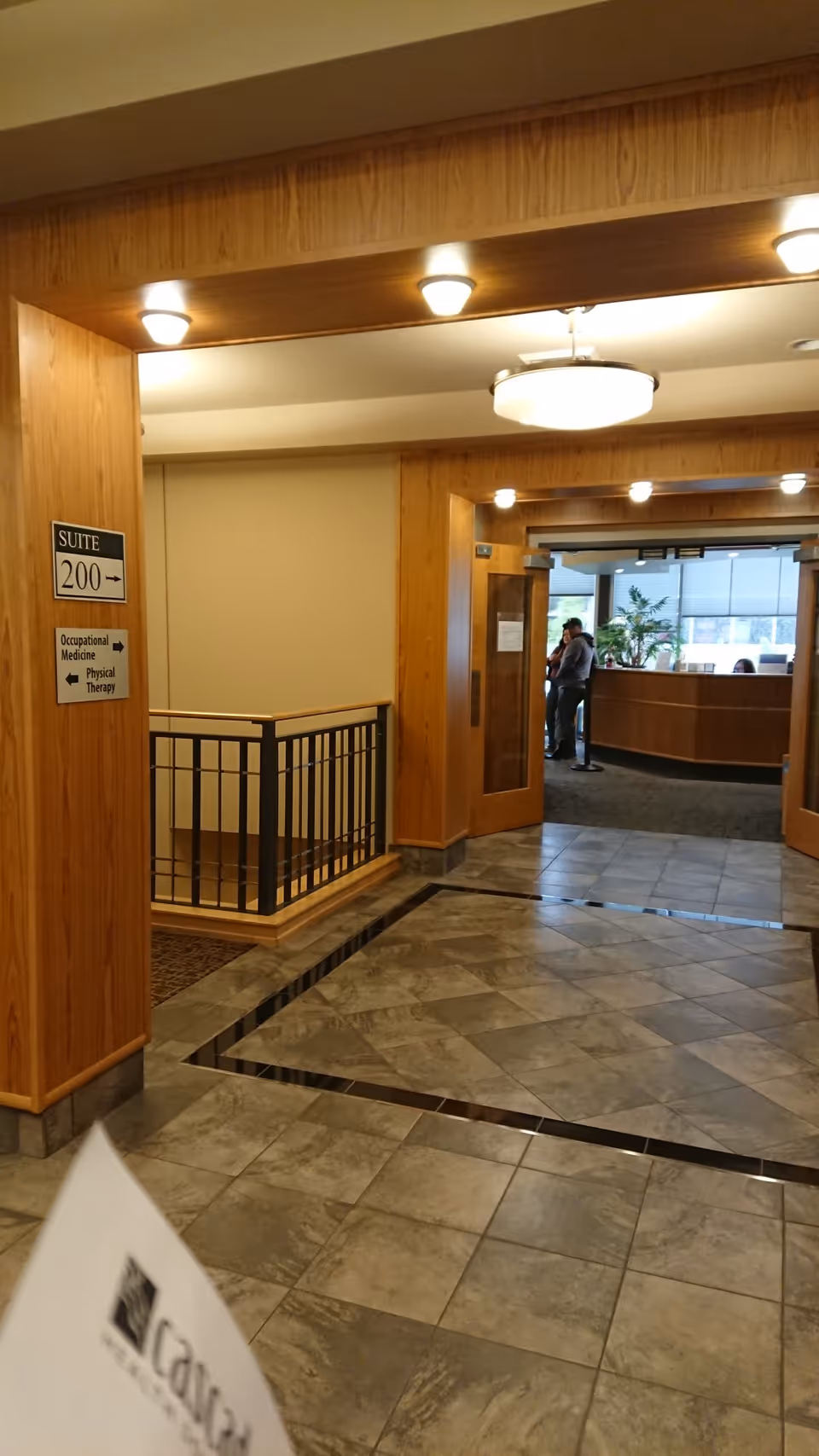 Cascade Health interior hallway with wood paneling, railing, and a reception area where two people stand.
