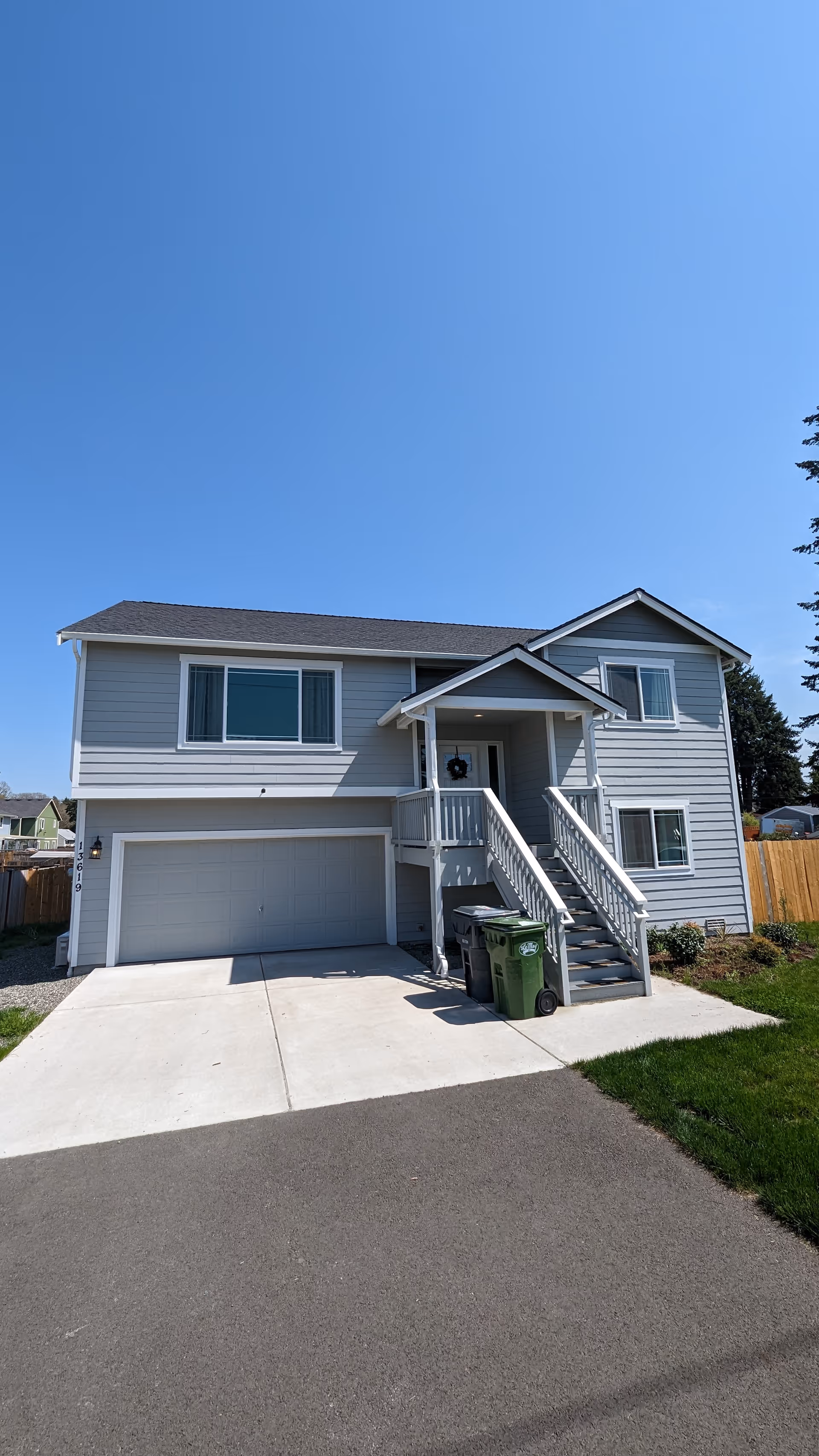 Two-story gray house with front porch, stairs, and a closed garage door on bright day.