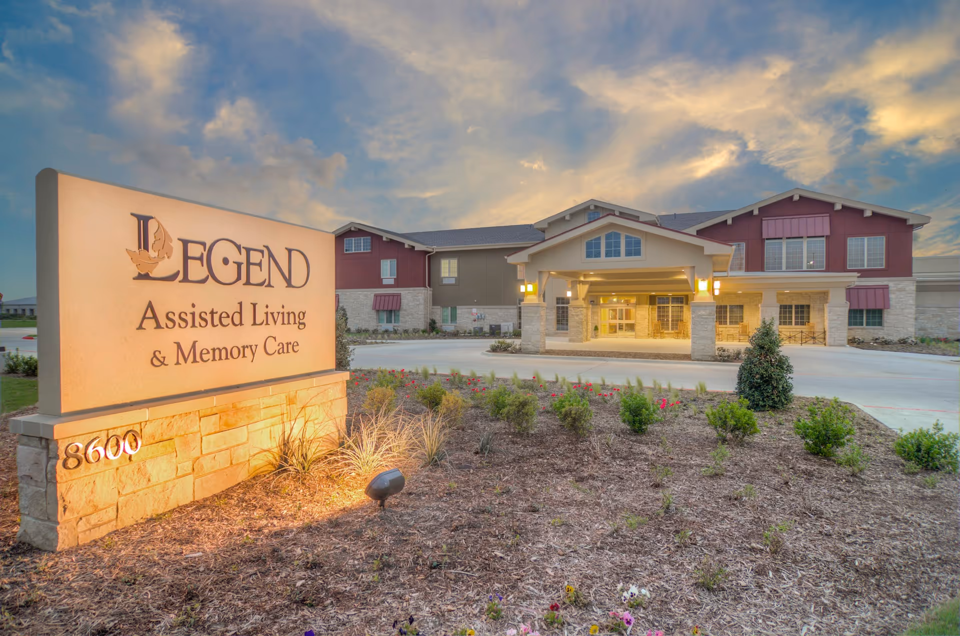 Exterior view of Legend Assisted Living building with illuminated entrance and landscaped front.