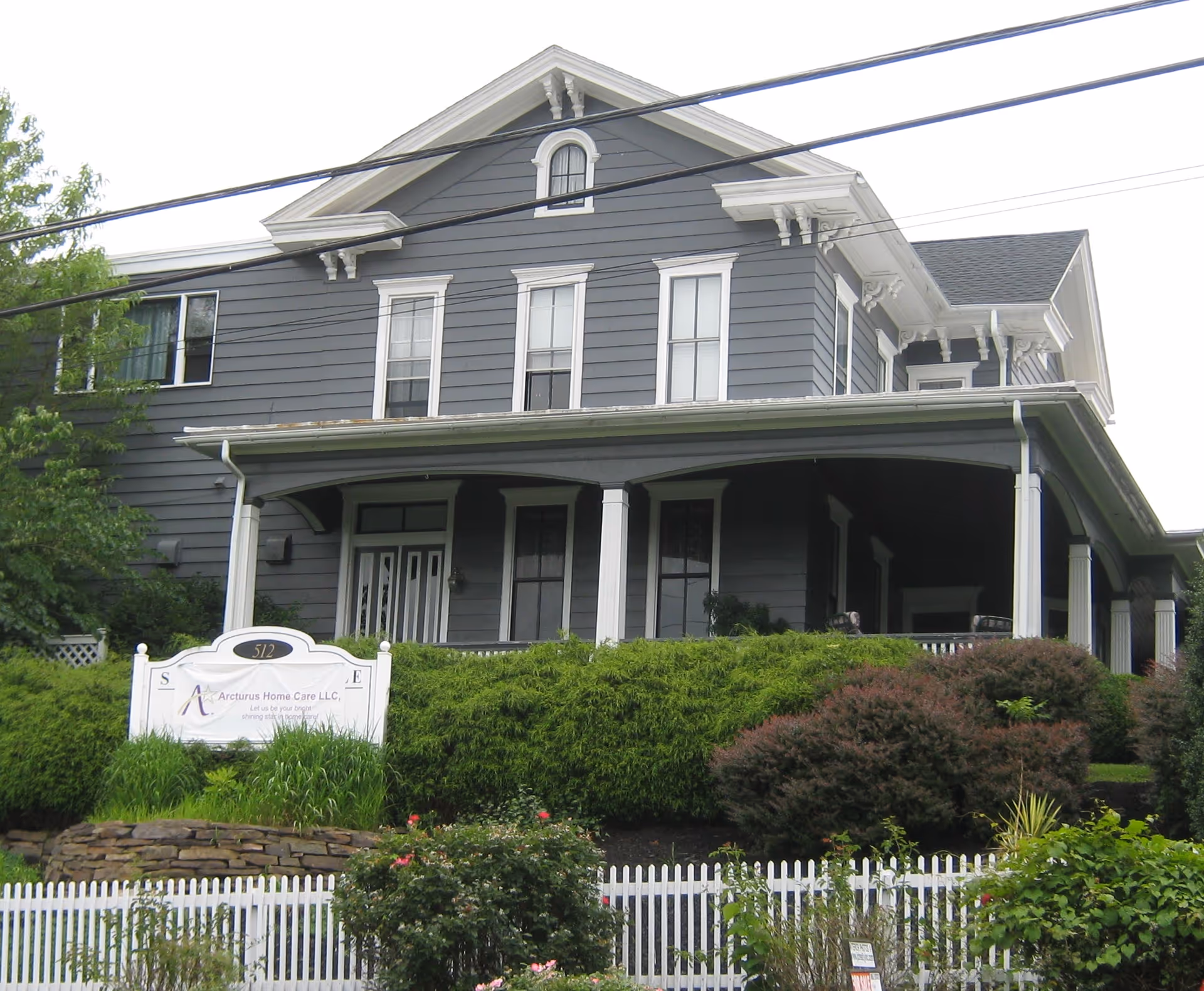 Grey two-story house with a covered porch and a sign for Arcturus Home Care LLC.