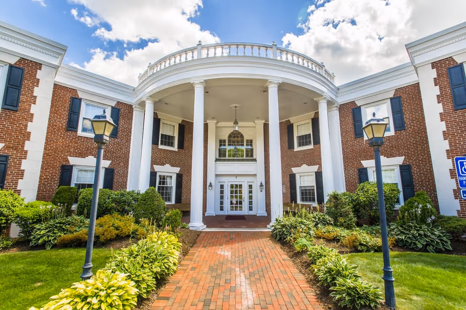 Brick building with a grand colonnaded entrance, brick walkway, and manicured landscaping.