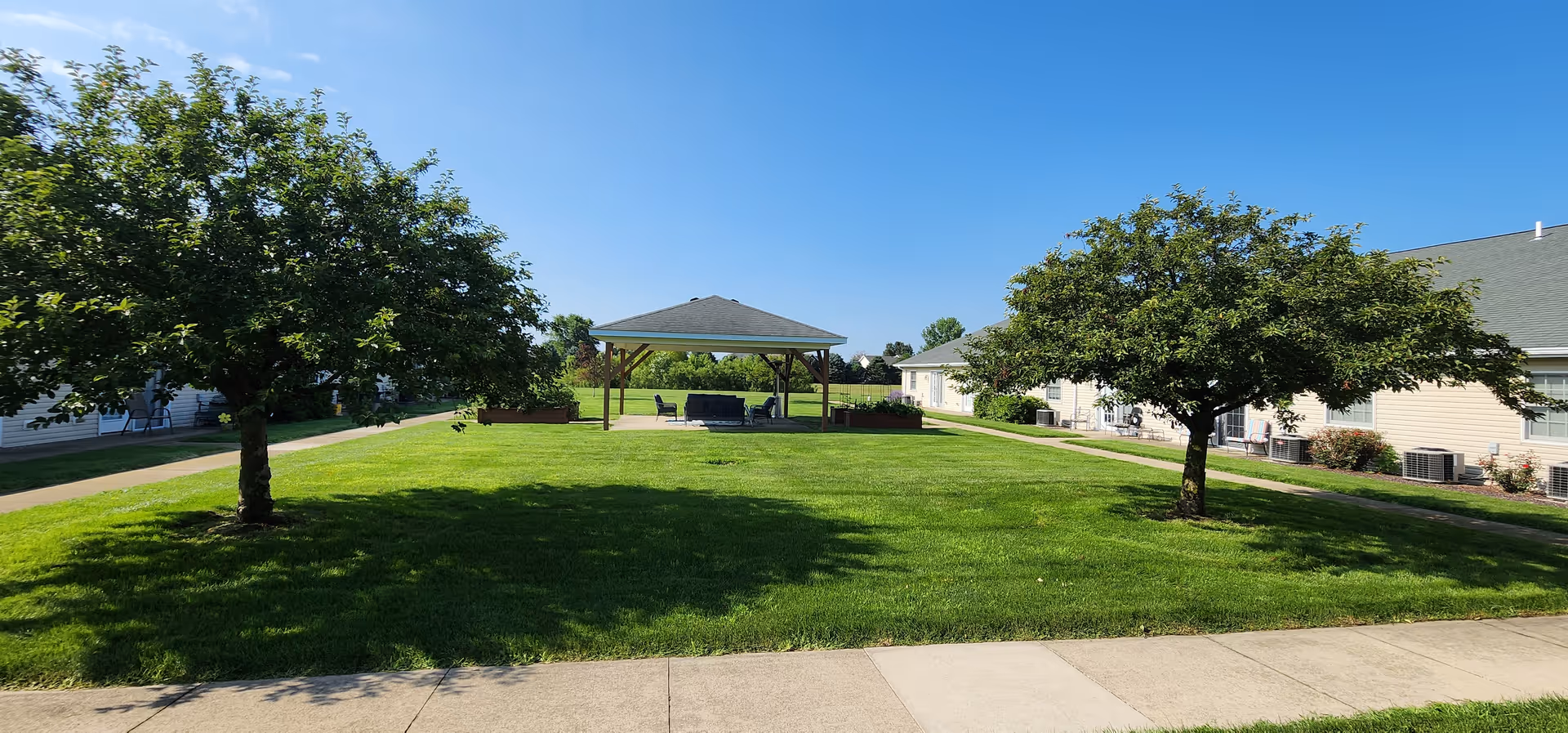 Sunny day at The Glenwood: green lawn, trees, and a gazebo near residential buildings.