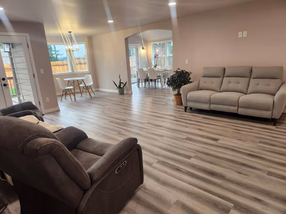 A spacious common area in a senior living facility featuring seating and a dining table.