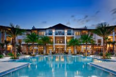 Exterior view of a senior living campus with a central pool and palm trees.
