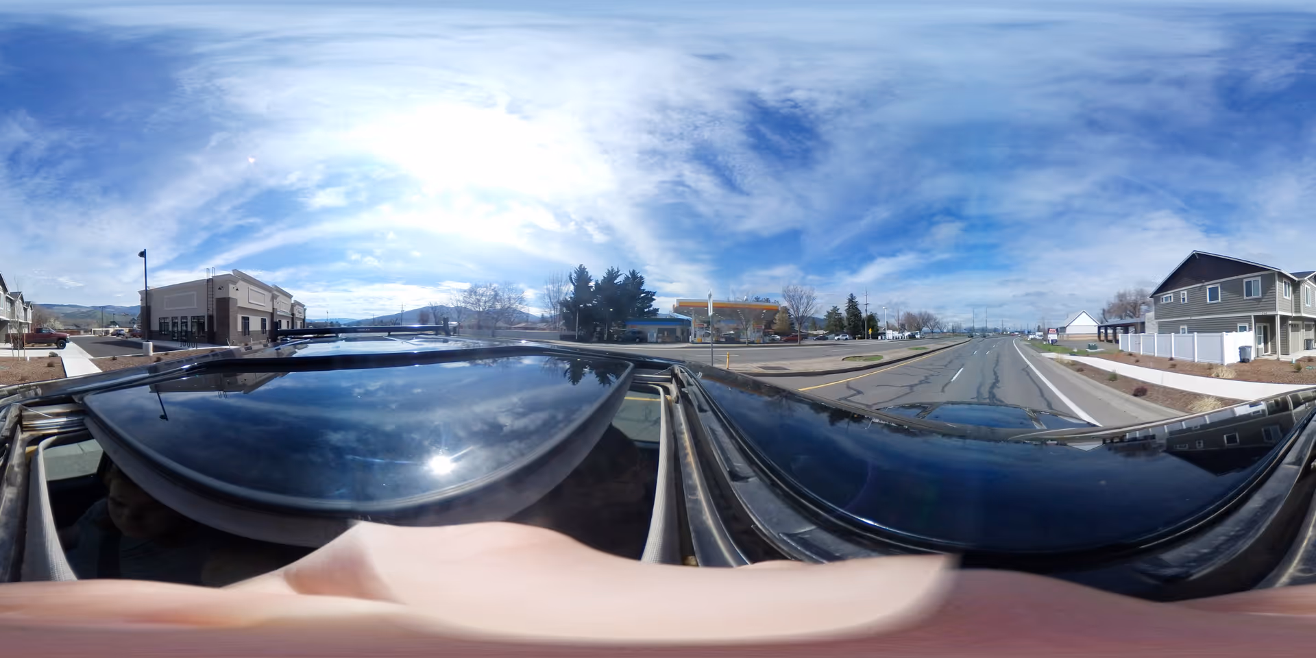 Panoramic exterior street view with buildings and a car roof in foreground.