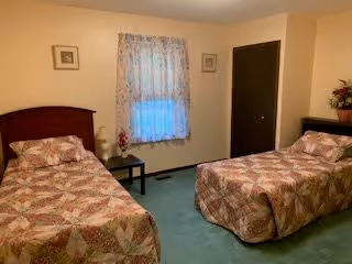 Two twin beds with floral bedspreads in a simple bedroom with a window and a small nightstand between them.