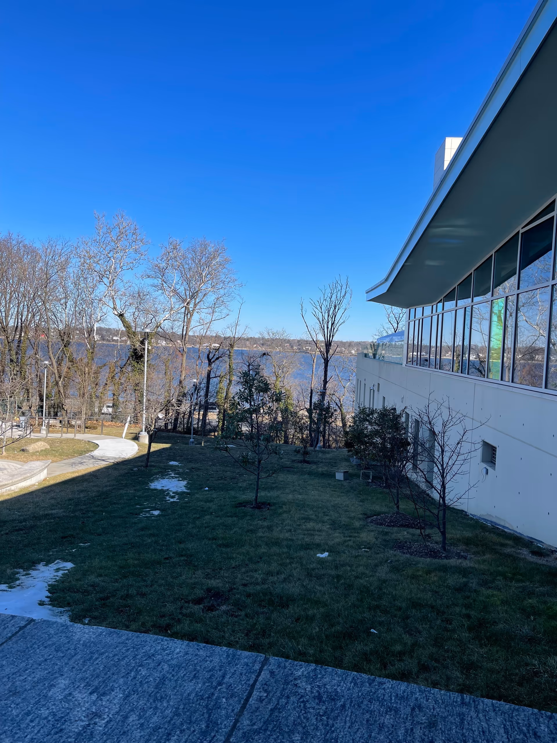 Exterior view of a modern facility with glass windows, trees, and a waterfront landscape.