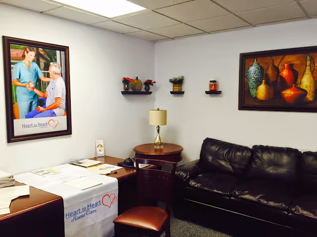 Indoor waiting area with black leather sofa, round table, lamp, and framed art.