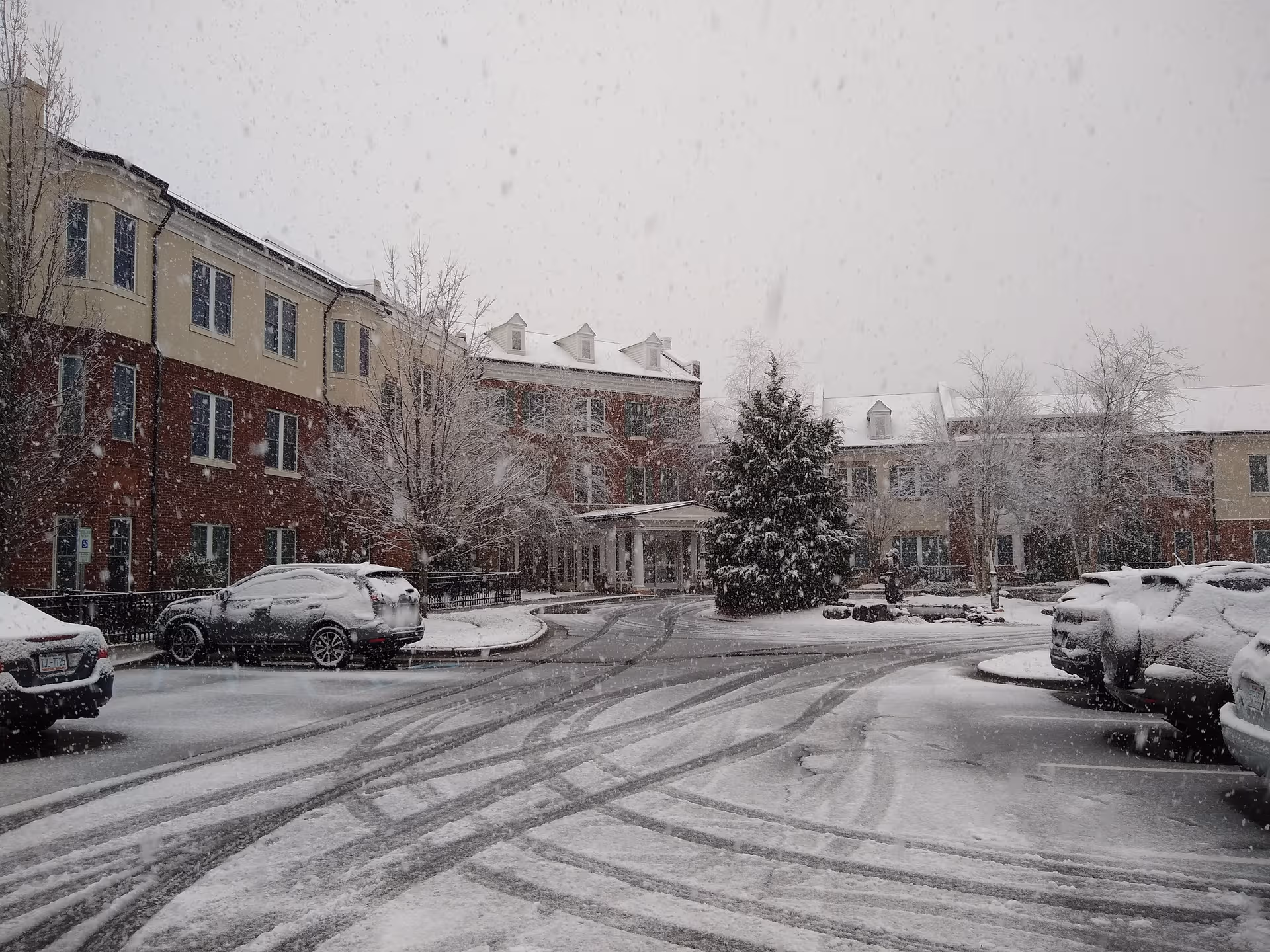 Exterior view of Arbor Acres - Asbury Place in snowfall with parked cars.