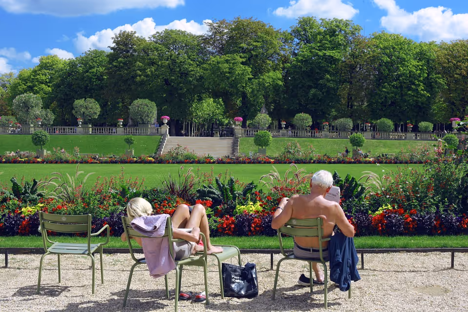 Two seniors relax in green chairs in a sunny, flower-filled outdoor garden.