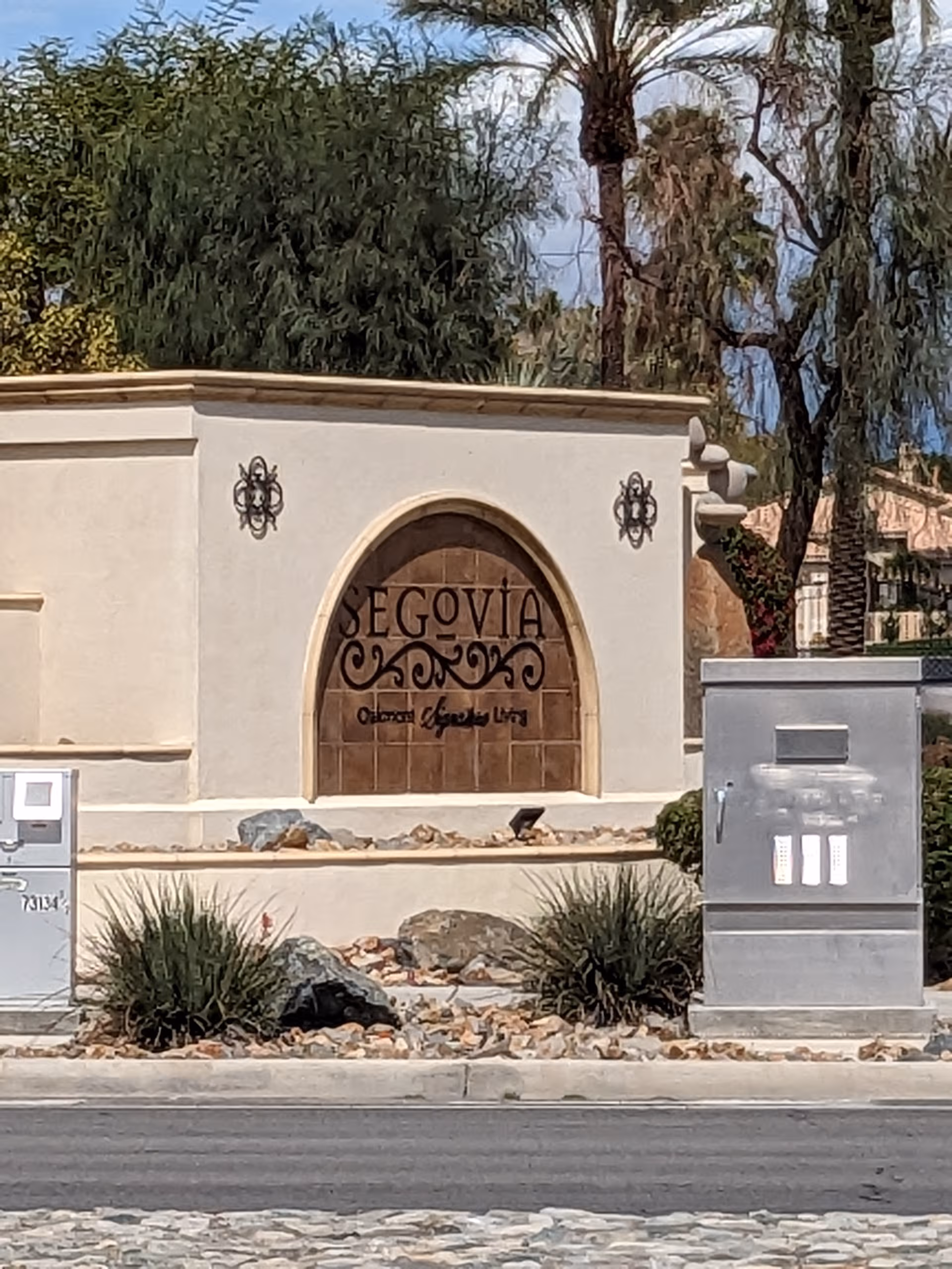 Stone entrance sign reading Segovia with desert landscaping and palm trees