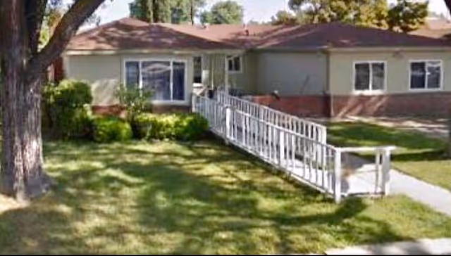 Front view of a single-story senior living home with a white ramp and green lawn.