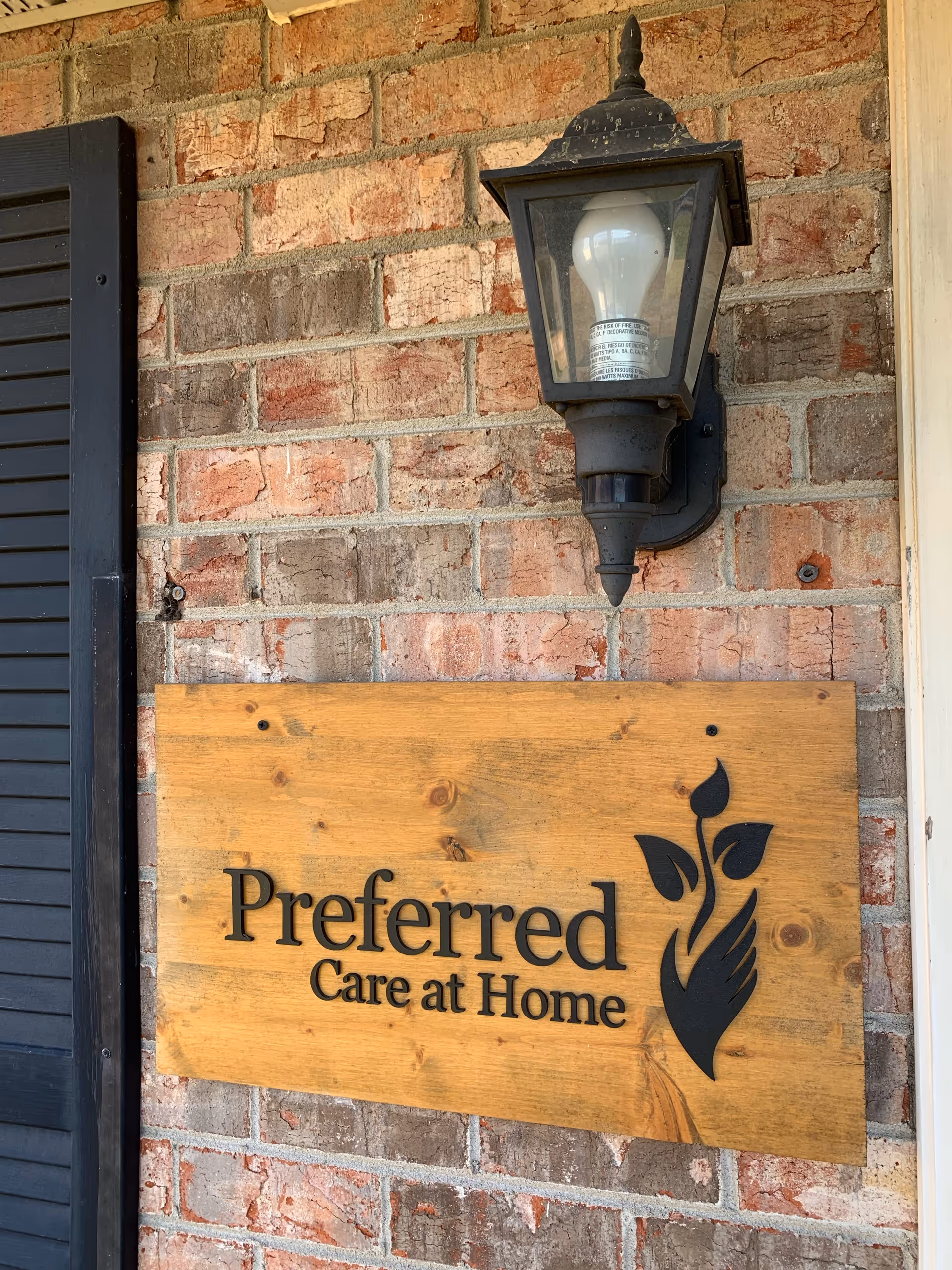 Exterior brick wall with a wooden sign reading 'Preferred Care at Home' and a lantern.