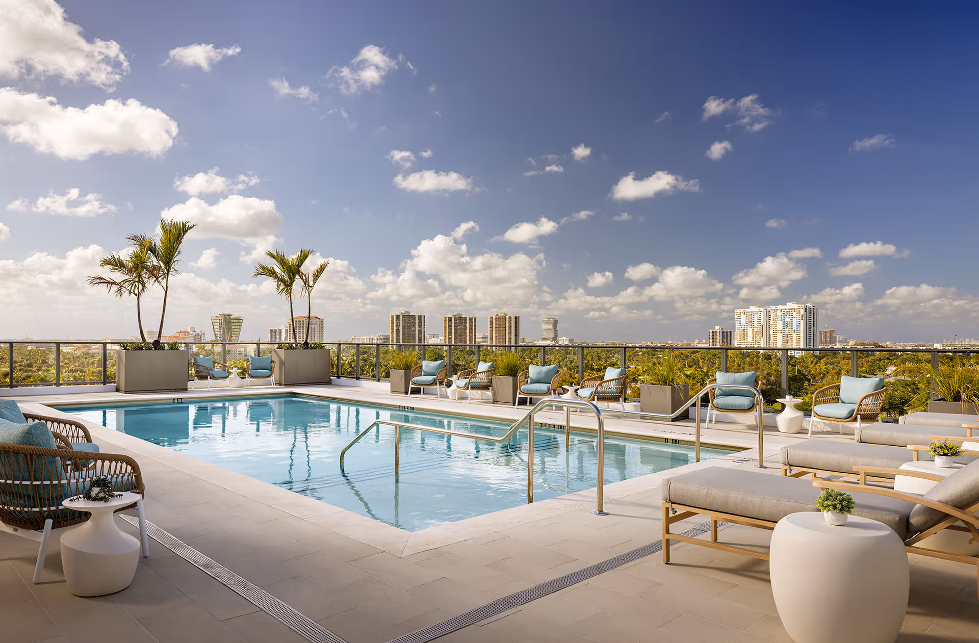Outdoor rooftop pool area with lounge chairs and palm trees overlooking city skyline.