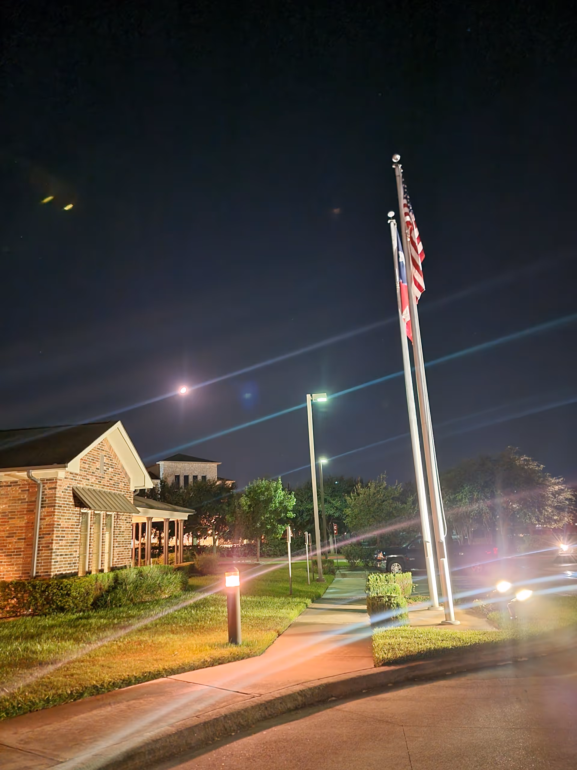 Night exterior view of The Crescent facility with flagpoles, a lit walkway, and landscaping.