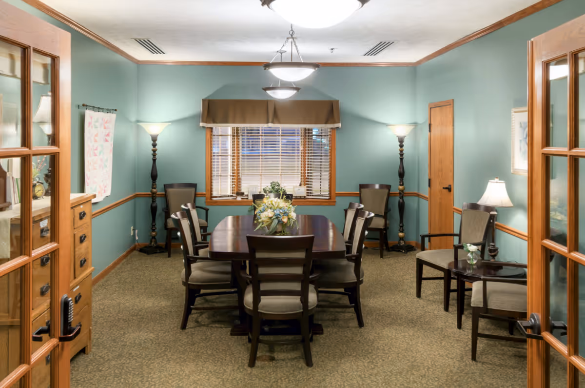Teal dining room with a wooden table, chairs, lamps, and a window.