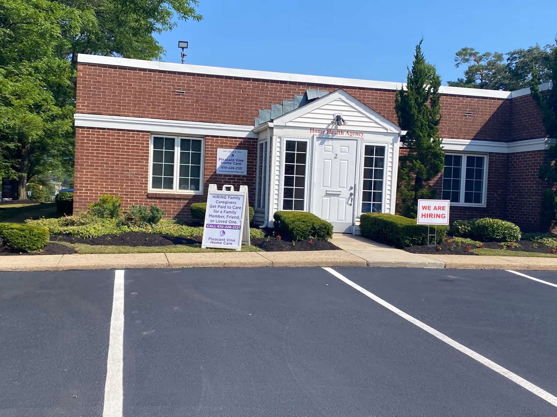 Brick building with a white entrance and multiple hiring signs in front landscaping.
