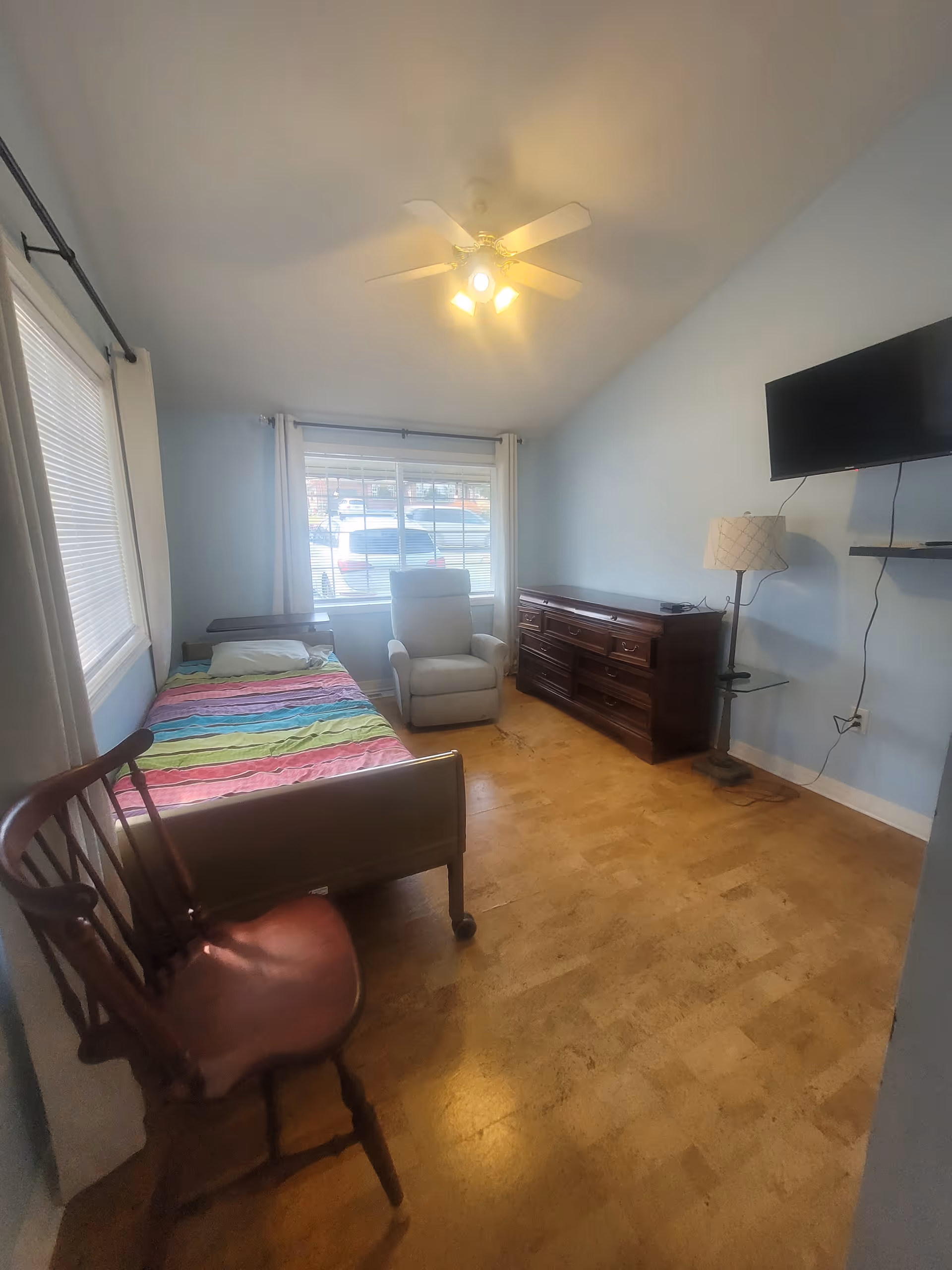 Small bedroom with a single bed, recliner, dresser, and wall-mounted TV.