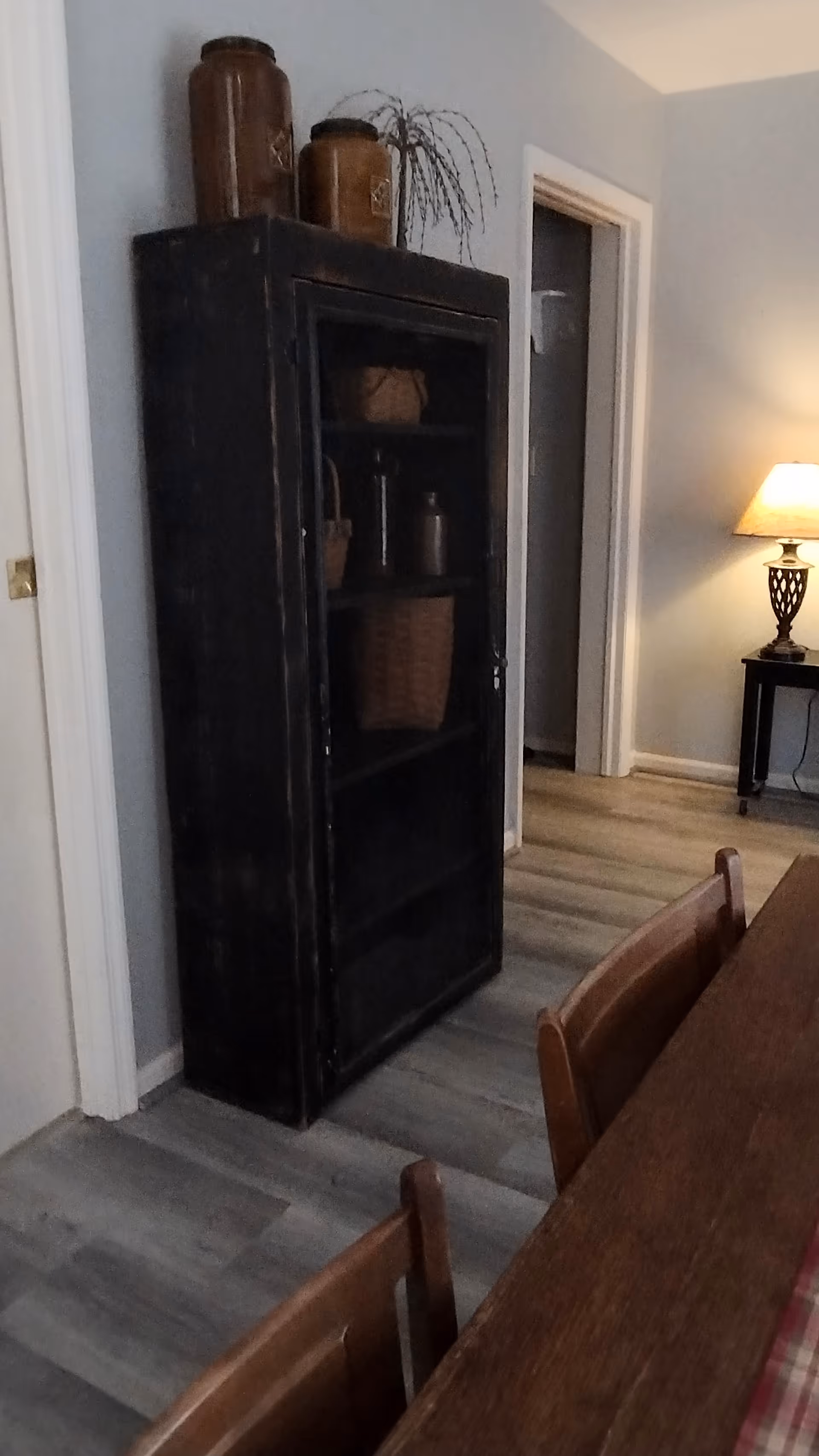 Dark cabinet beside dining table in a blue-walled dining area with lamp.