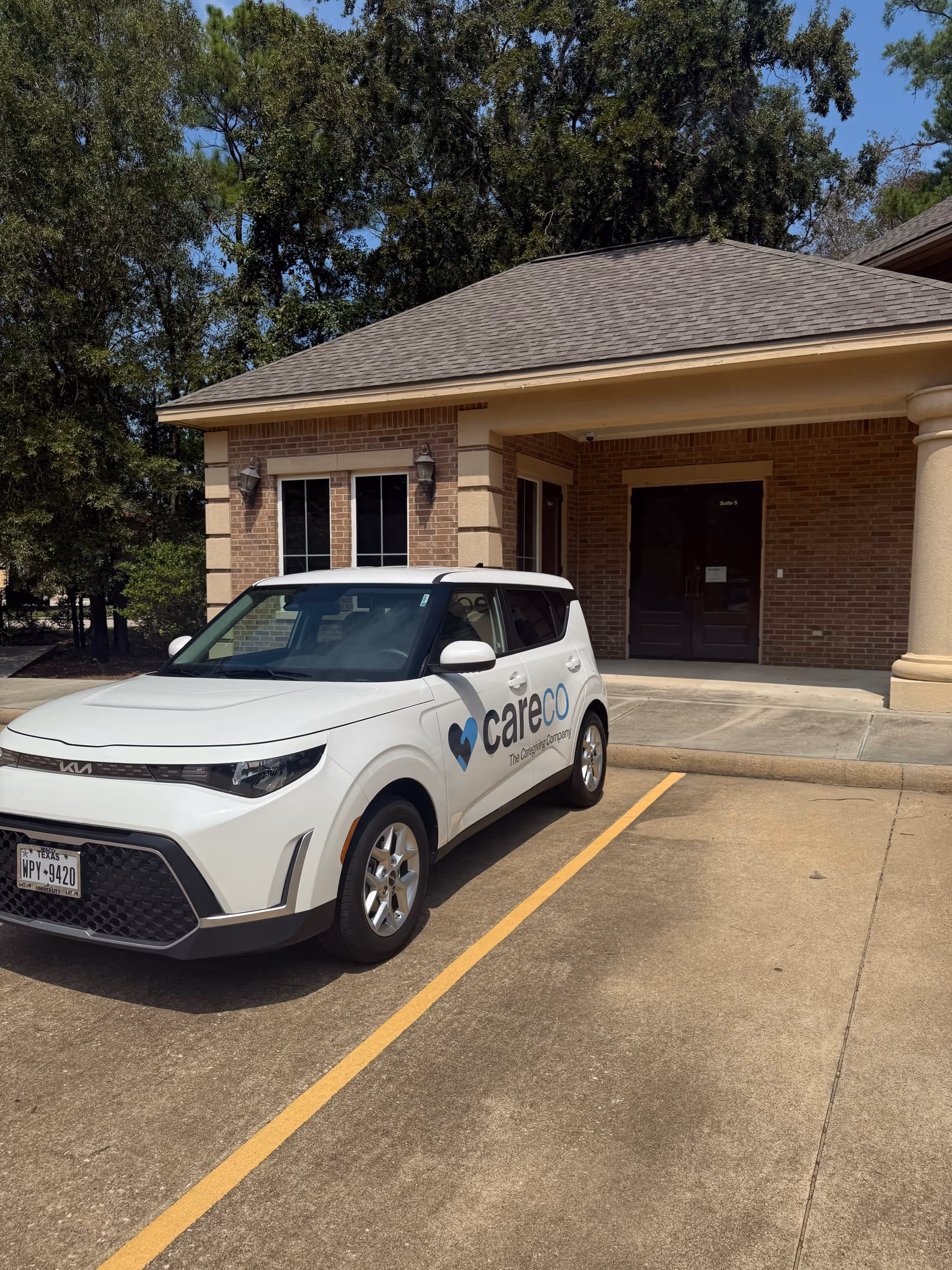 White CareCo vehicle parked outside brick senior homecare facility entrance.
