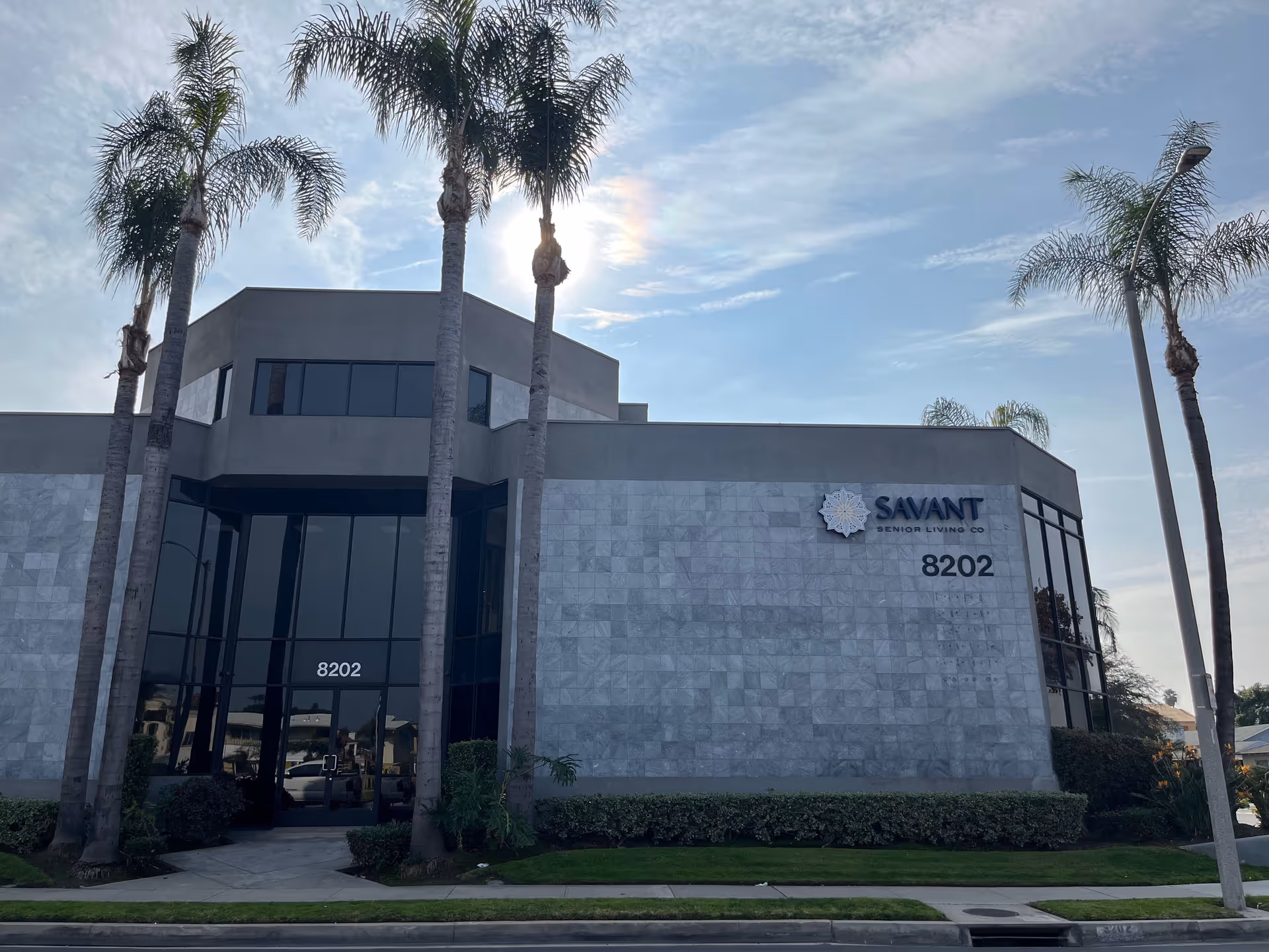 Modern Savant Senior Living building with glass entry, stone facade, and palm trees.