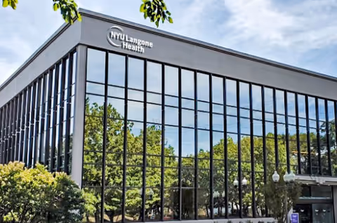 Modern glass-front building with NYU Langone Health signage and surrounding greenery.