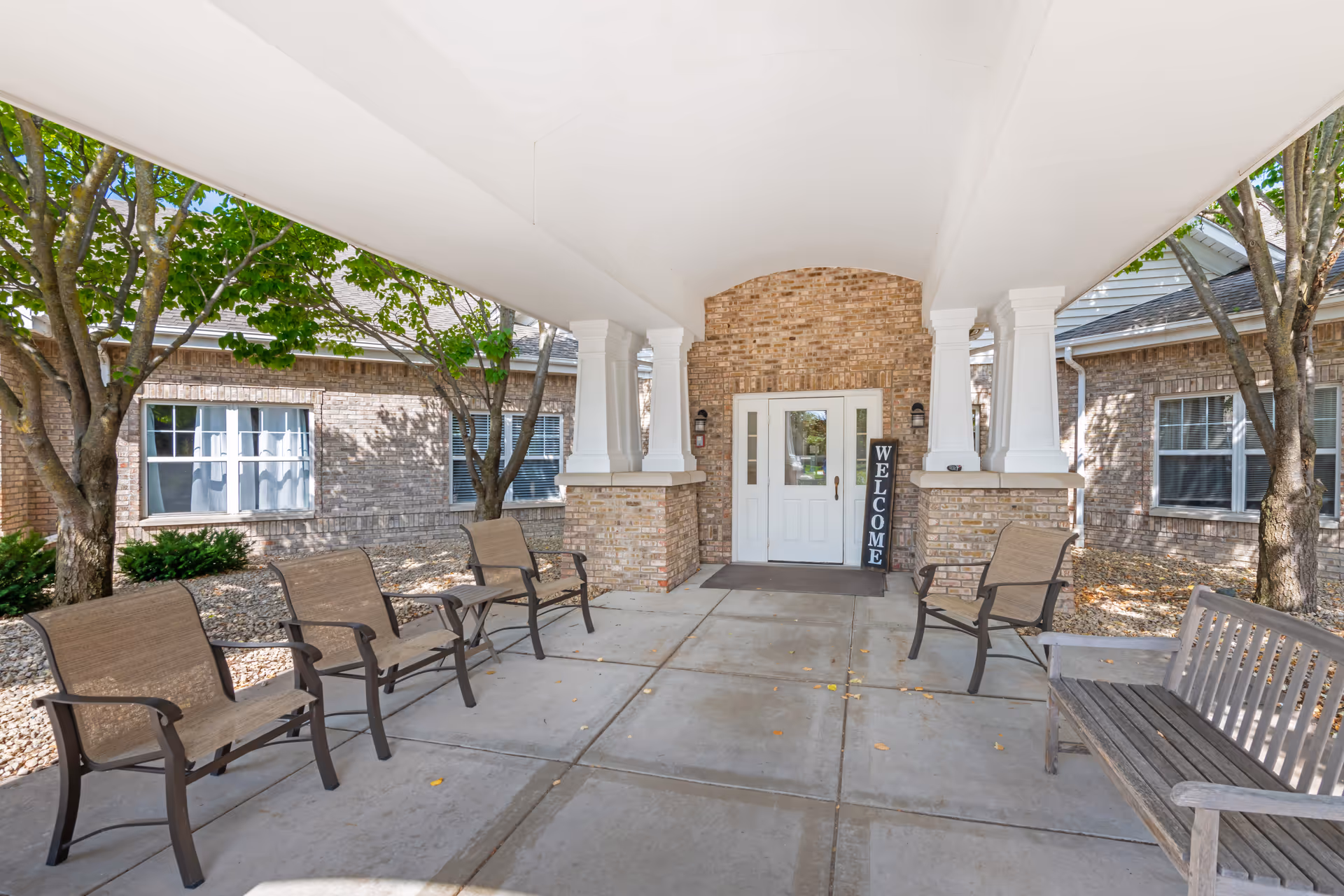 Covered brick entrance with white columns, benches, and a welcome sign at Brookdale North Oaks