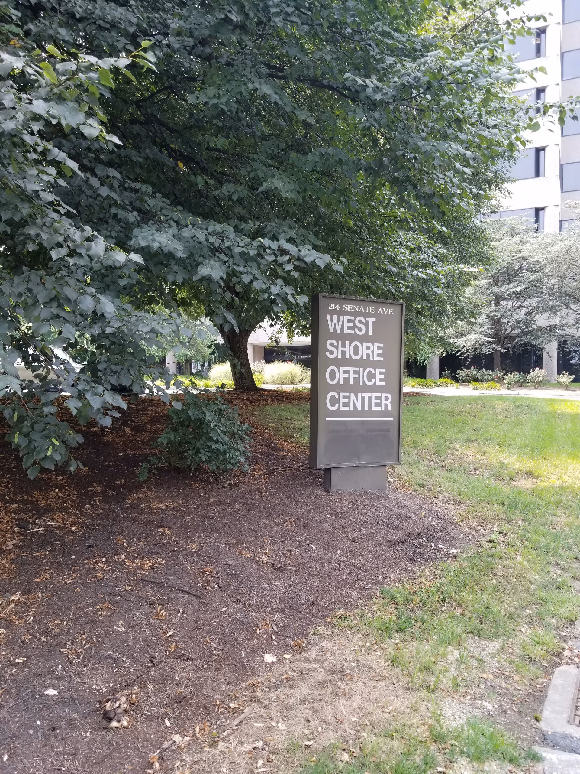 Outdoor view of West Shore Office Center sign beside a building and trees.
