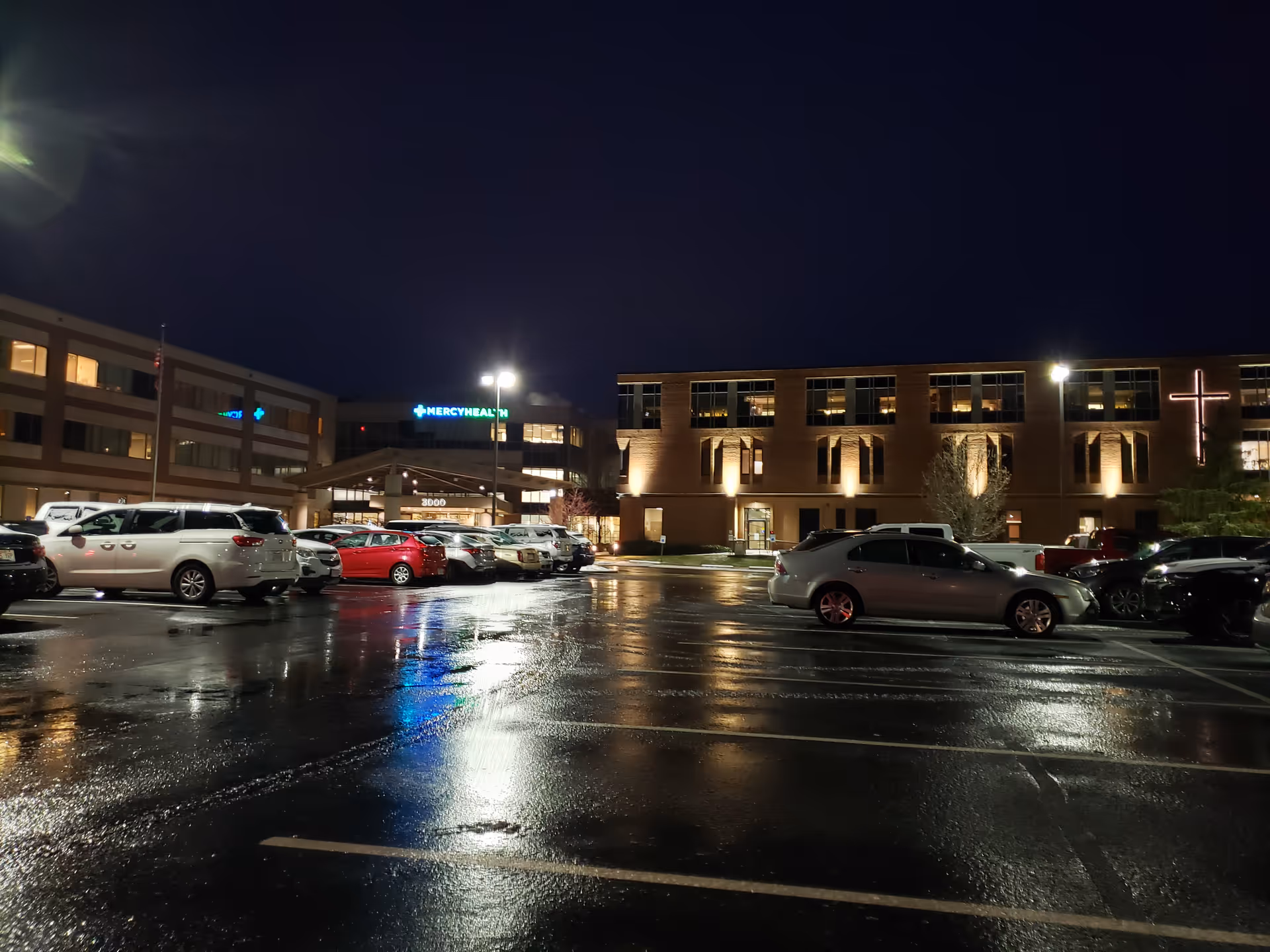 Night exterior view of Mercy Health Clermont Hospital, with a wet parking lot and illuminated building.