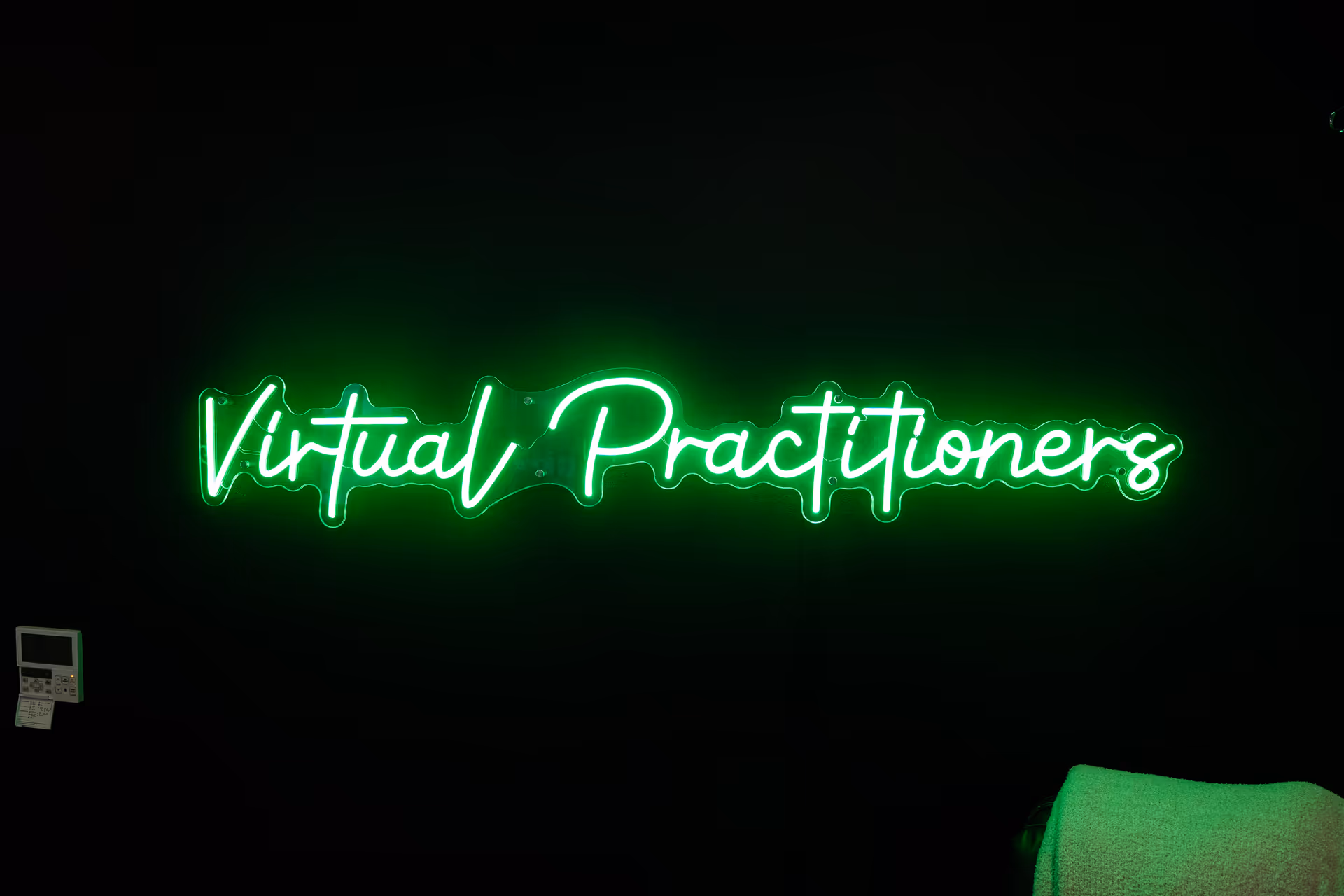 Green neon sign reading 'Virtual Practitioners' on a dark interior wall.