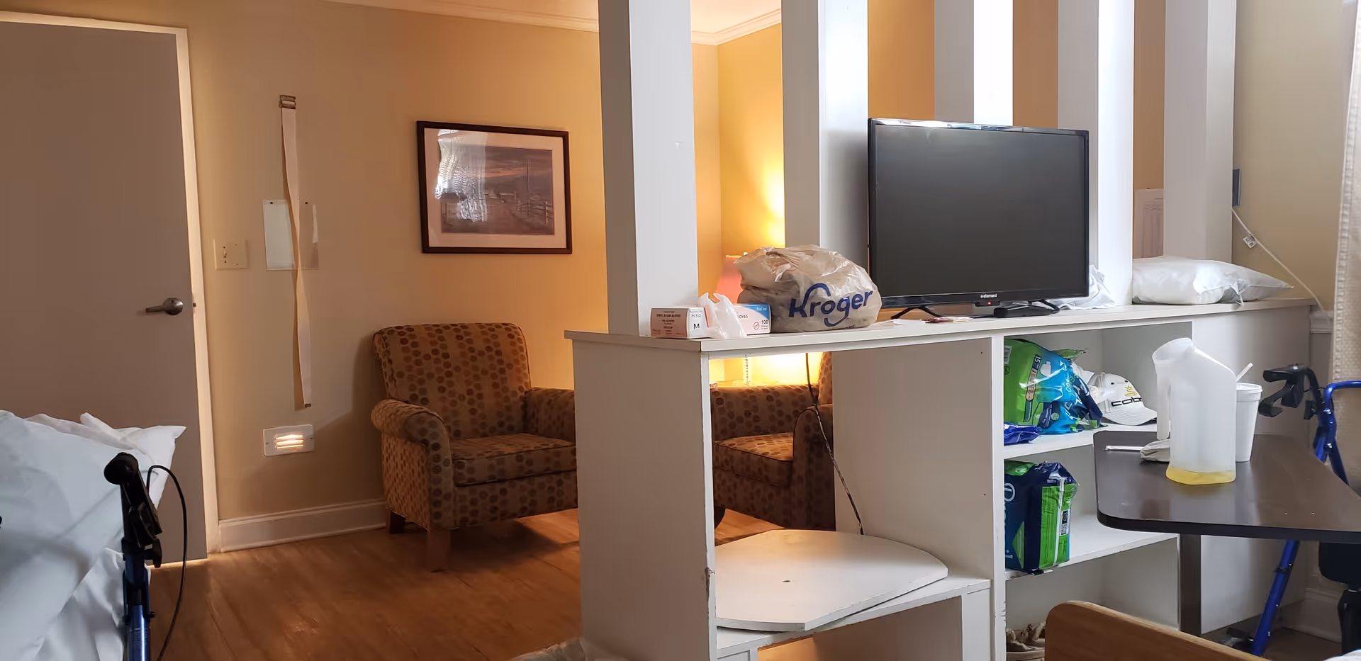 Interior view of a hospital-style patient room with TV, chairs, and medical supplies.