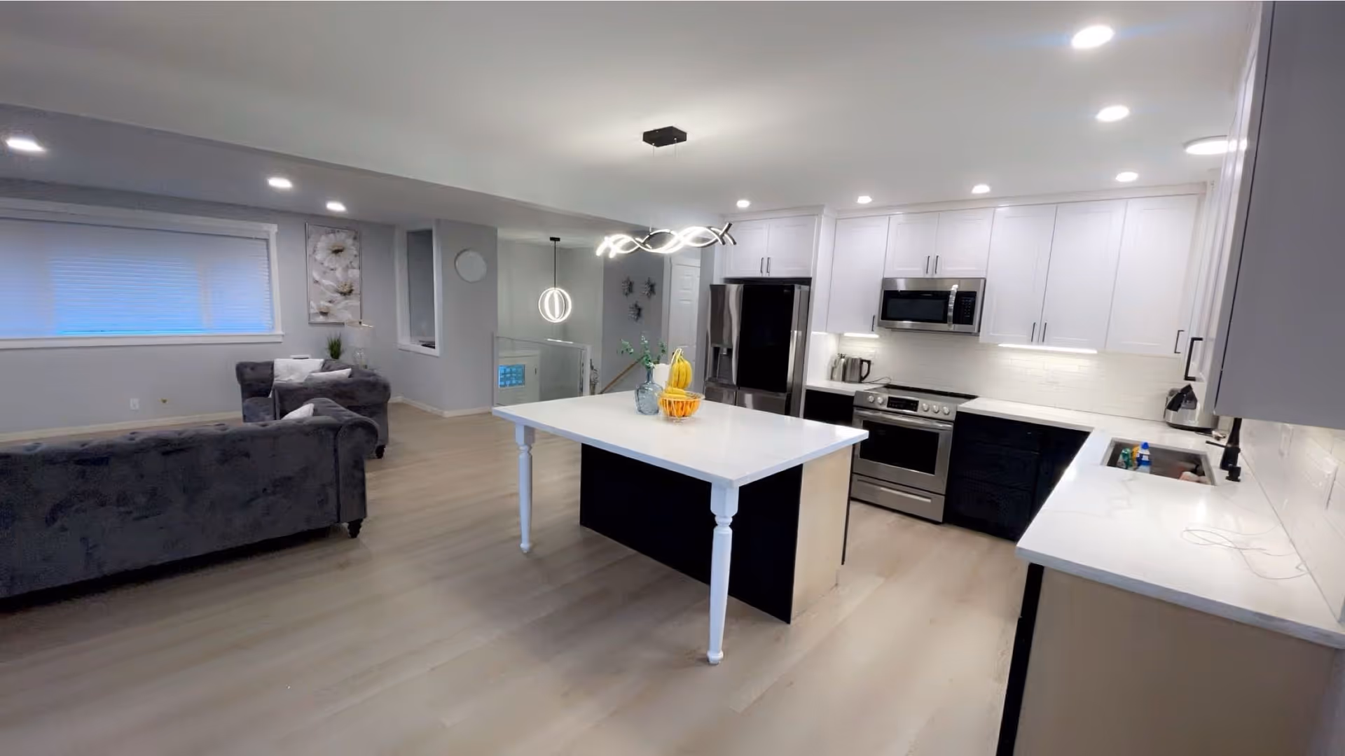 Open-concept kitchen and living area with a white island, stainless appliances, and gray seating.