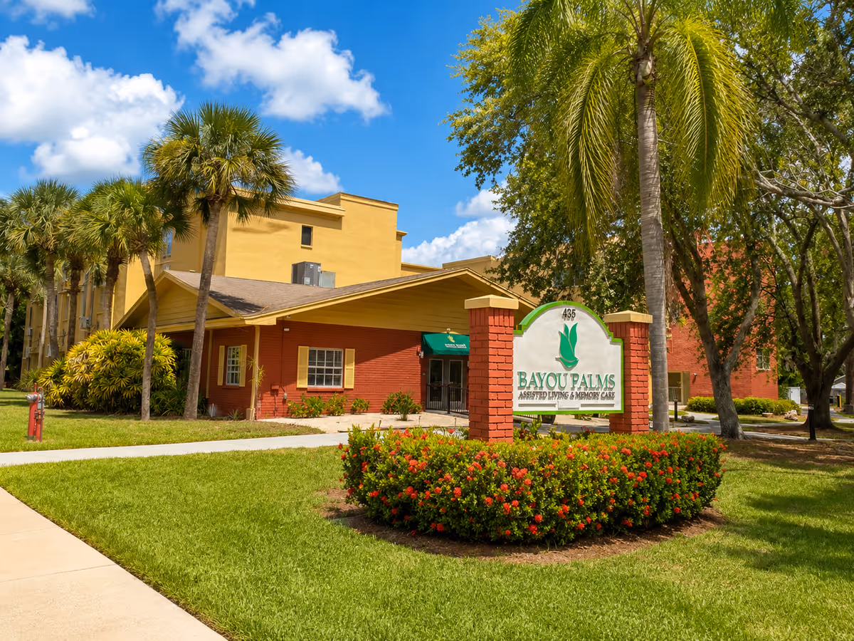 Exterior view of Bayou Palms Assisted Living & Memory Care with sign and landscaping.
