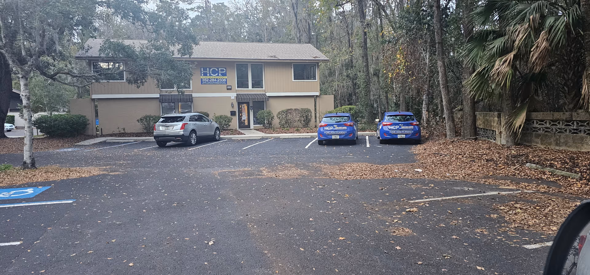 Two blue HCP vehicles parked in front of a tan, two-story Home Healthcare Agency building.