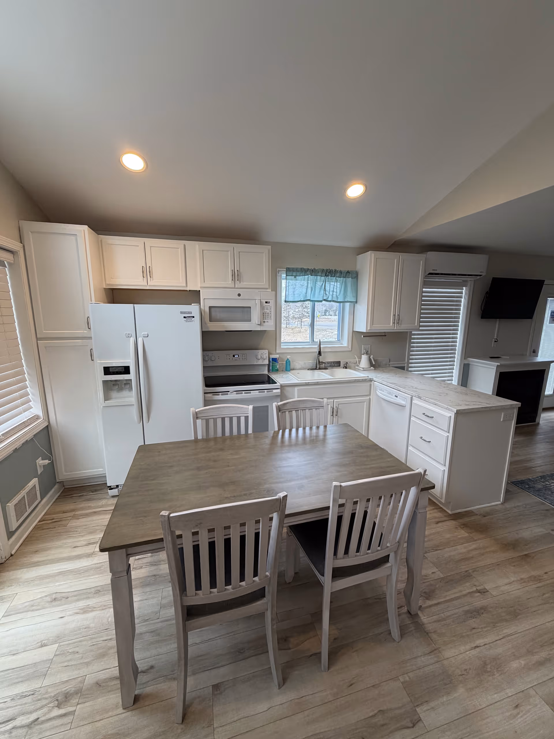 White kitchen with appliances surrounds a wooden dining table and four chairs.