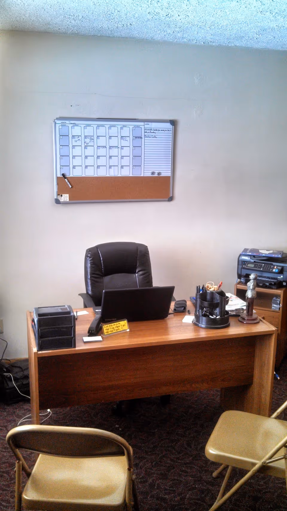 Office desk with laptop, calendar board, and chairs in a staff area.
